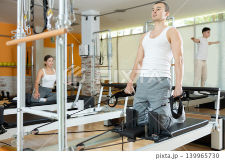 Man performing exercises with straps on Pilates reformer during rehabilitation workout Man performing exercises with straps on Pilates reformer during rehabilitation workout 139965730