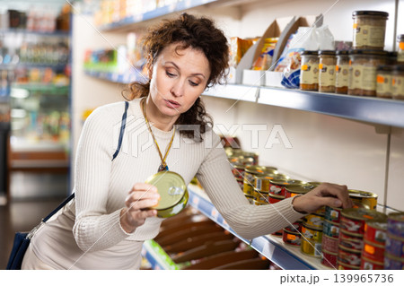 Adult woman chooses sprats in store Adult woman chooses sprats in store 139965736