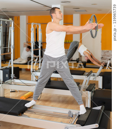 Man stands on reformer and holds ring, hoop in his hands, performs exercises to balance Man stands on reformer and holds ring, hoop in his hands, performs exercises to balance 139965739