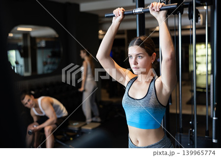 Slender athletic girl work out muscles of arms and shoulders on simulator in gym of fitness club 139965774