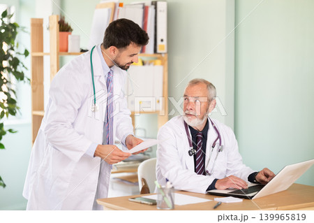 Adult and elderly male doctors working on laptop discussing test results 139965819