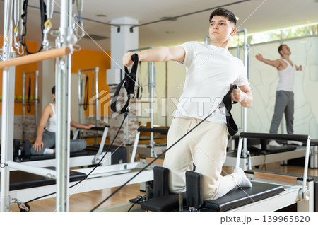 Man in gym with help of rope reformer performs exercises to strengthen muscles of arms Man in gym with help of rope reformer performs exercises to strengthen muscles of arms 139965820