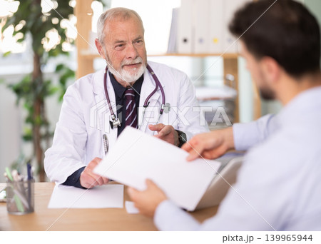 Senior male doctor and man patient examine papers, discuss medical tests result. Senior male doctor and man patient examine papers, discuss medical tests result. 139965944