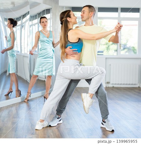 Couple in comfortable sports clothes learns tango dancing during individual lesson Couple in comfortable sports clothes learns tango dancing during individual lesson 139965955