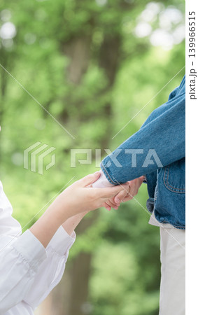 新緑の自然の中で笑顔で手を繋ぐ見つめ合う、触れ合う親子の子育てイメージ 手元のクローズアッ顔無しの縦 新緑の自然の中で笑顔で手を繋ぐ見つめ合う、触れ合う親子の子育てイメージ 手元のクローズアッ顔無しの縦 139966515