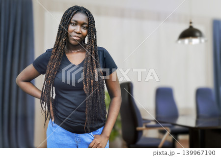 Confident young Black woman with long braids standing in a modern corporate office meeting room 139967190