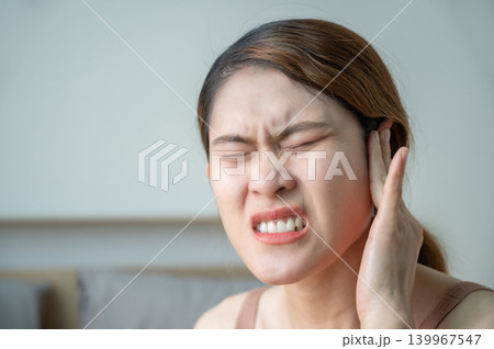 Asian woman having an earache problem. An earache is sharp, dull, or burning ear pain in one or both ears. 139967547