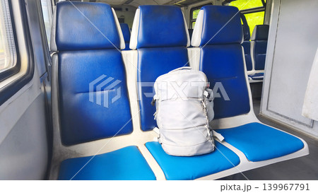 A gray backpack on blue seats inside a commuter train car during a daytime commute. Urban transportation, car interior in Ukraine. Train ride 139967791