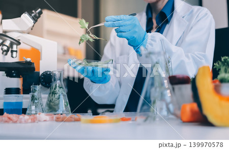 Scientists in lab coats work with plants in a modern lab, focusing on research and experimentation under bright, sterile conditions. Scientists in lab coats work with plants in a modern lab, focusing on research and experimentation under bright, sterile conditions. 139970578