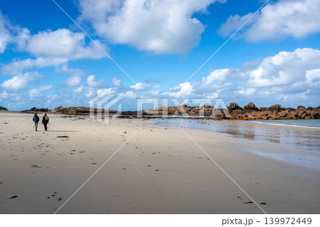 Walkers crossing Coz Pors beach toward granite reef in Brittany, France 139972449