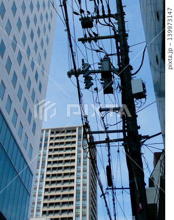 都会のビル群と複雑に交差する電柱・電線 139973147