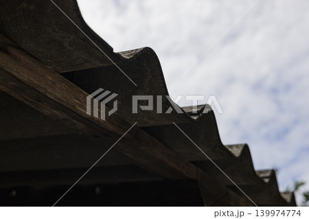 Concrete Roof Tiles Installed On A Wooden Frame Structure. Close up of gray house roofing material on timber beams against bright sky, ideal for construction or architectural design themes. Concrete Roof Tiles Installed On A Wooden Frame Structure. Close up of gray house roofing material on timber beams against bright sky, ideal for construction or architectural design themes. 139974774