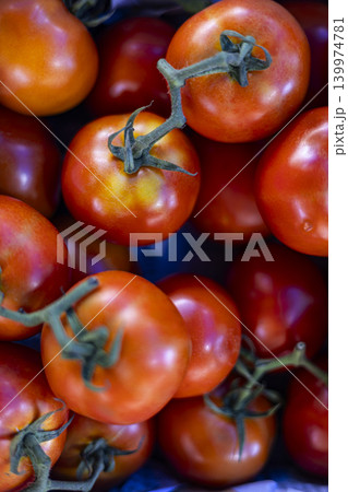Pile Tomatoes Display Market Stall Fresh Vegetable. Close up of ripe red tomatoes with green stems stacked on local grocery shop counter, perfect for healthy diet or organic farming themes. 139974781