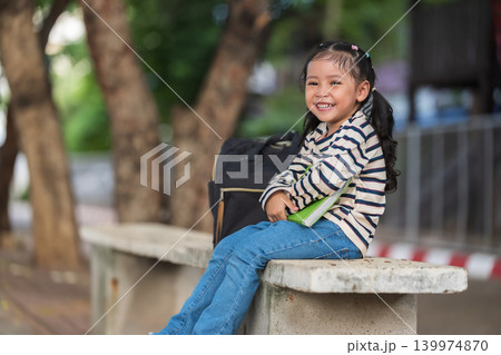 happy child girl sitting on a concrete bench outdoors of school, reading a book. Education and learning concept. happy child girl sitting on a concrete bench outdoors of school, reading a book. Education and learning concept. 139974870