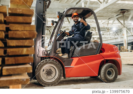 Warehouse worker operating a forklift while handling wooden materials Warehouse worker operating a forklift while handling wooden materials 139975670