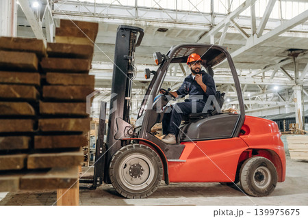Heavy material, lifting the planks. Warehouse worker operating a forklift while handling wooden materials 139975675