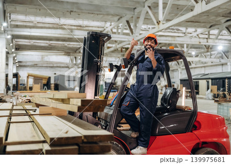 Transportation of the planks. Warehouse worker operating a forklift while handling wooden materials Transportation of the planks. Warehouse worker operating a forklift while handling wooden materials 139975681
