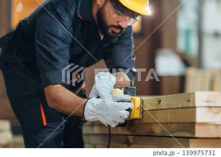 In protective hardhat. Male carpenter working with wooden materials in a professional workshop In protective hardhat. Male carpenter working with wooden materials in a professional workshop 139975731