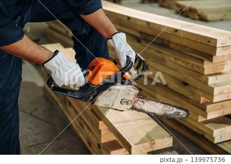 Using a chainsaw. Close-up of a carpenter working with wood using professional tools in a workshop Using a chainsaw. Close-up of a carpenter working with wood using professional tools in a workshop 139975736