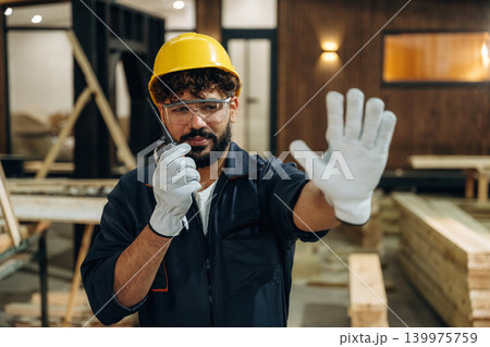 Talking by walkie talkie. Portrait of a male carpenter posing in a woodworking workshop Talking by walkie talkie. Portrait of a male carpenter posing in a woodworking workshop 139975759