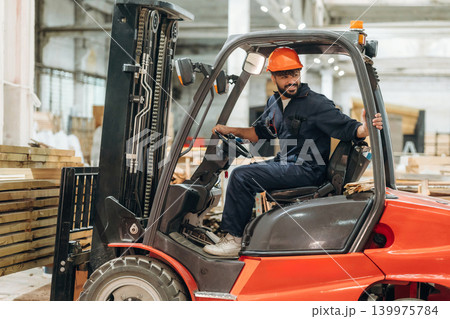 Driving, skilled employee. Warehouse worker operating a forklift while handling wooden materials Driving, skilled employee. Warehouse worker operating a forklift while handling wooden materials 139975784