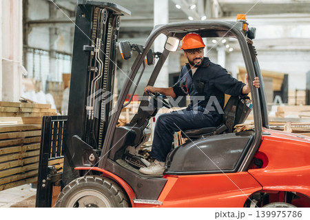Driving, skilled employee. Warehouse worker operating a forklift while handling wooden materials Driving, skilled employee. Warehouse worker operating a forklift while handling wooden materials 139975786