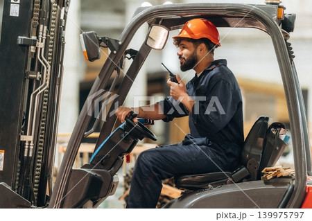Ready to load. Warehouse worker operating a forklift while handling wooden materials Ready to load. Warehouse worker operating a forklift while handling wooden materials 139975797