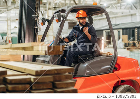 Ready to load. Warehouse worker operating a forklift while handling wooden materials Ready to load. Warehouse worker operating a forklift while handling wooden materials 139975803