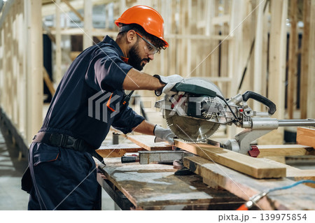View from the side, cutting the wood. Male carpenter working with materials in a professional workshop View from the side, cutting the wood. Male carpenter working with materials in a professional workshop 139975854