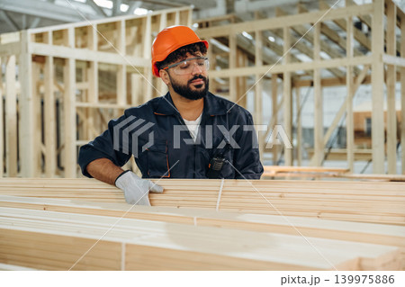 Bunch of new planks. Male carpenter working with wooden materials in a professional workshop Bunch of new planks. Male carpenter working with wooden materials in a professional workshop 139975886
