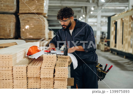 Writing on the paper, engineer is with plan. Male carpenter working with wooden materials in a professional workshop Writing on the paper, engineer is with plan. Male carpenter working with wooden materials in a professional workshop 139975893