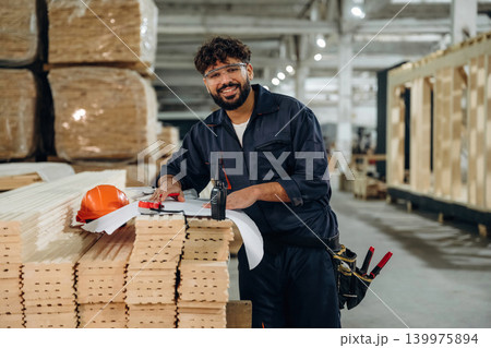 Writing on the paper, engineer is with plan. Male carpenter working with wooden materials in a professional workshop Writing on the paper, engineer is with plan. Male carpenter working with wooden materials in a professional workshop 139975894