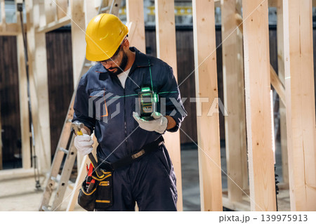 Leveler device is in hands. Male carpenter working with wooden materials in a professional workshop Leveler device is in hands. Male carpenter working with wooden materials in a professional workshop 139975913