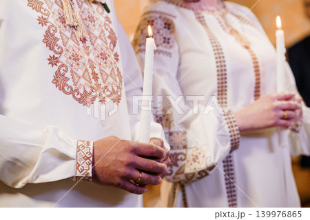 Bride and Groom in Traditional Embroidered White Outfits Holding Lit Wax Candles at Wedding Ceremony Bride and Groom in Traditional Embroidered White Outfits Holding Lit Wax Candles at Wedding Ceremony 139976865