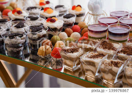 Assorted Gourmet Dessert Cups and Sweet Pastries Arranged on Gold Buffet Table for Event Catering Assorted Gourmet Dessert Cups and Sweet Pastries Arranged on Gold Buffet Table for Event Catering 139976867