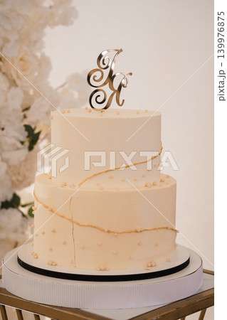 Two Tier White Cream Wedding Cake with Gold Initials Topper and Pearl Decor on White Backdrop Two Tier White Cream Wedding Cake with Gold Initials Topper and Pearl Decor on White Backdrop 139976875