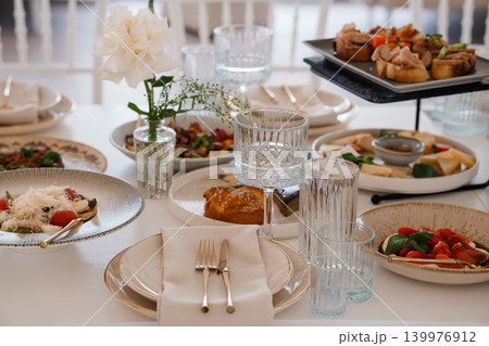 Elegant Fine Dining Table Setting with Appetizers, White Flowers, and Crystal Glassware in Bright Light Elegant Fine Dining Table Setting with Appetizers, White Flowers, and Crystal Glassware in Bright Light 139976912