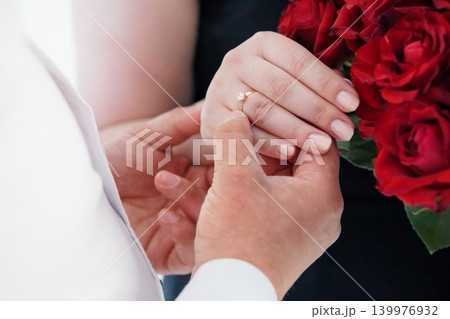 Close Up of Couple Exchanging Wedding Rings with Red Roses Bouquet in Romantic Setting Close Up of Couple Exchanging Wedding Rings with Red Roses Bouquet in Romantic Setting 139976932