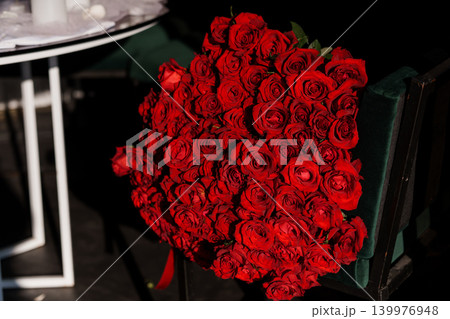 Large Bouquet of Deep Red Roses Resting on a Dark Green Velvet Chair in Elegant Interior Setting 139976948
