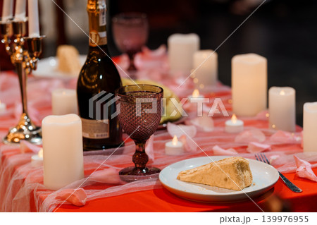 Romantic Dinner Setting with Red Tablecloth, Wine, White Candles, and Rose Petals on a Table Romantic Dinner Setting with Red Tablecloth, Wine, White Candles, and Rose Petals on a Table 139976955