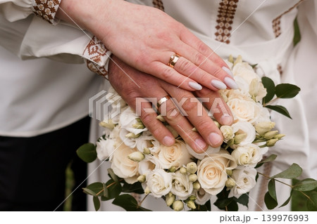 Close up of Couple Hands with Wedding Rings over White Rose Bouquet in Elegant Bridal Style 139976993