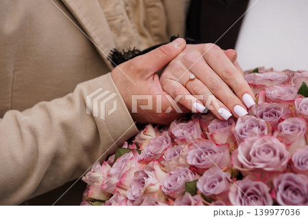 Close Up of Hands Holding Pink Roses with Diamond Engagement Ring in Beige Blazer Close Up of Hands Holding Pink Roses with Diamond Engagement Ring in Beige Blazer 139977036