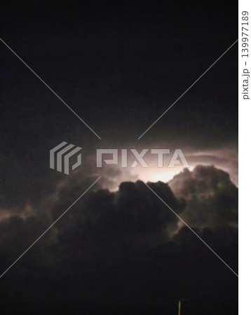 A dark, moody storm cloud formation at night with a bright illuminated edge, capturing an intense and dramatic atmosphere before a thunderstorm A dark, moody storm cloud formation at night with a bright illuminated edge, capturing an intense and dramatic atmosphere before a thunderstorm 139977189
