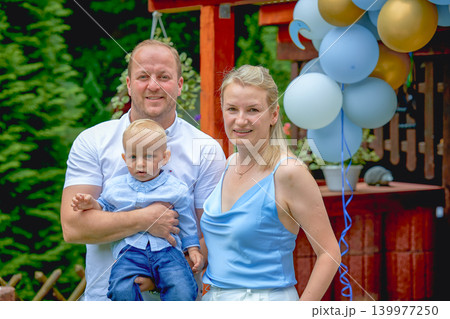 mom dad and baby one year old family photo outside in summer on a sunny day, family of European appearance all blondes dressed in blue clothes baby and dad with blue eyes. High quality photo 139977250