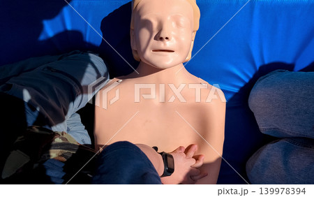 A professional paramedic teacher is teaching a boy first aid and CPR training for kids using a medical mannequin. This outdoor workshop focuses on practicing chest compressions A professional paramedic teacher is teaching a boy first aid and CPR training for kids using a medical mannequin. This outdoor workshop focuses on practicing chest compressions 139978394