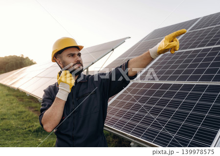 Giving orders by talking by walkie talkie. Male solar engineer examining photovoltaic panels at a power station 139978575