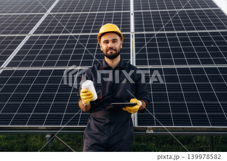 Break time, with drink. Male solar engineer examining photovoltaic panels at a power station Break time, with drink. Male solar engineer examining photovoltaic panels at a power station 139978582