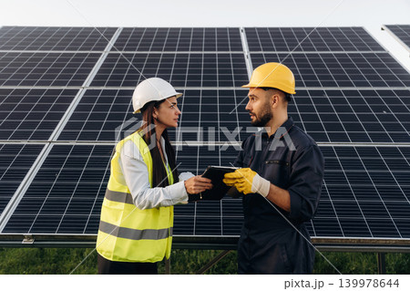 Two solar engineers standing together at a photovoltaic field, in bright safety vests Two solar engineers standing together at a photovoltaic field, in bright safety vests 139978644