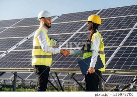Handshake, cooperation, success. Two solar engineers standing together at a photovoltaic field, in bright safety vests Handshake, cooperation, success. Two solar engineers standing together at a photovoltaic field, in bright safety vests 139978700