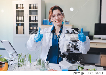 Scientists in lab coats work with plants in a modern lab, focusing on research and experimentation under bright, sterile conditions. 139978711